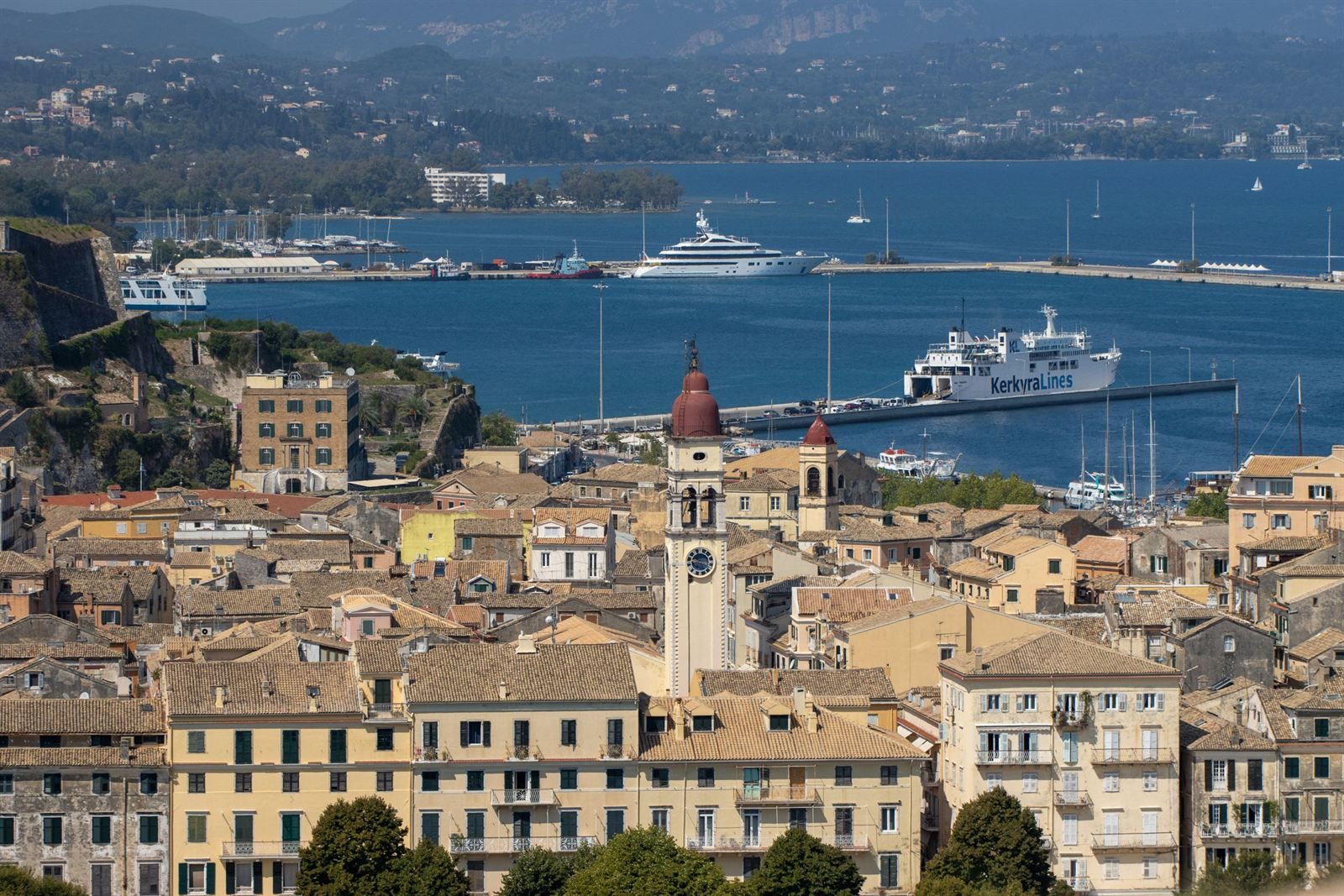 Rooftops of Corfu Town and a red-domed bell tower, with ferries and yachts in the harbor behind