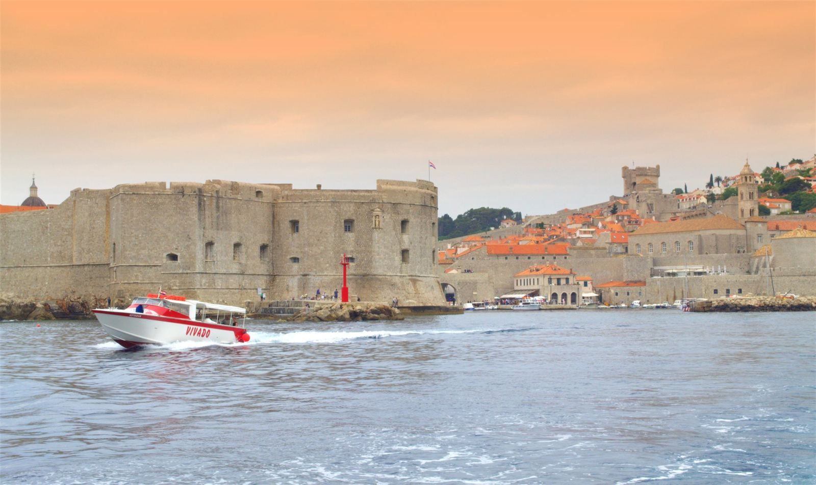 A small boat speeding past the stone fortress and harbor walls of Dubrovnik&rsquo;s Old Town