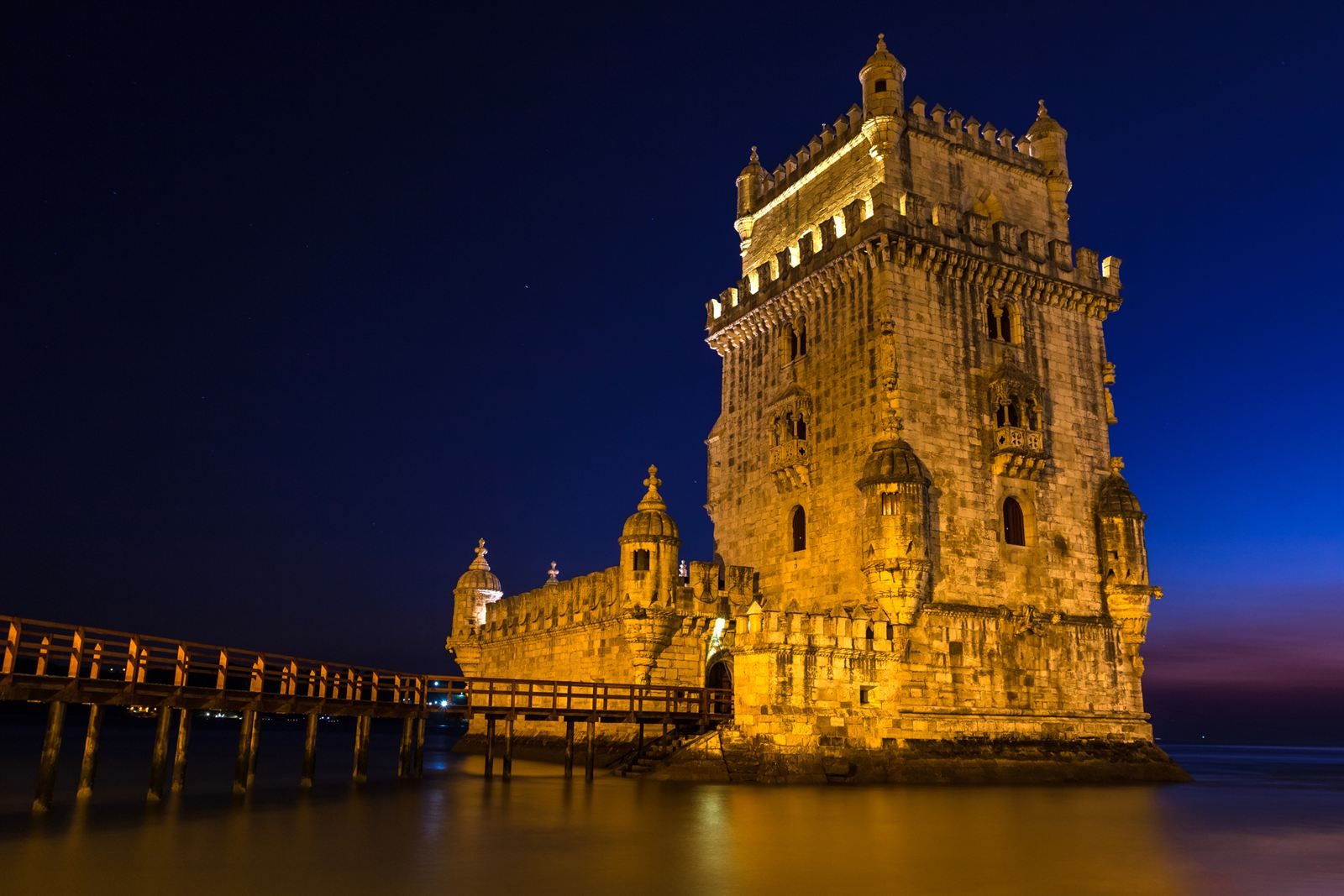 Belém Tower lit up at night on the Tagus River in Lisbon, with its wooden footbridge