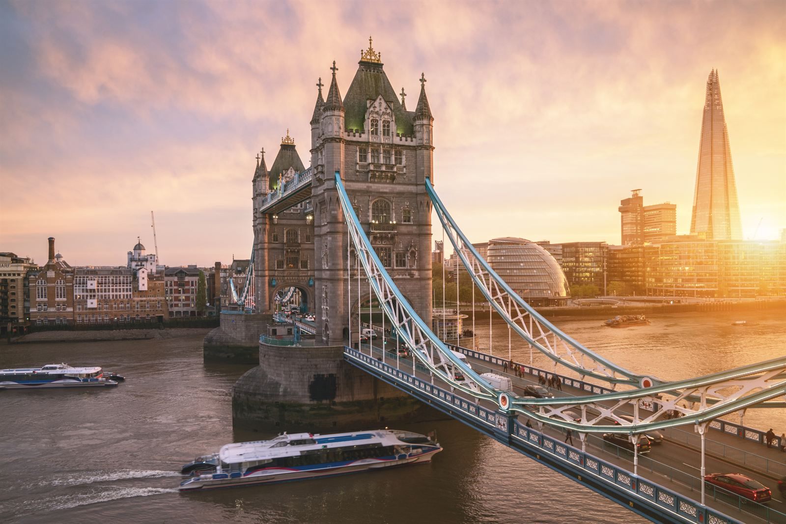 Tower Bridge over the Thames at sunset, with a riverboat below and the Shard in the background