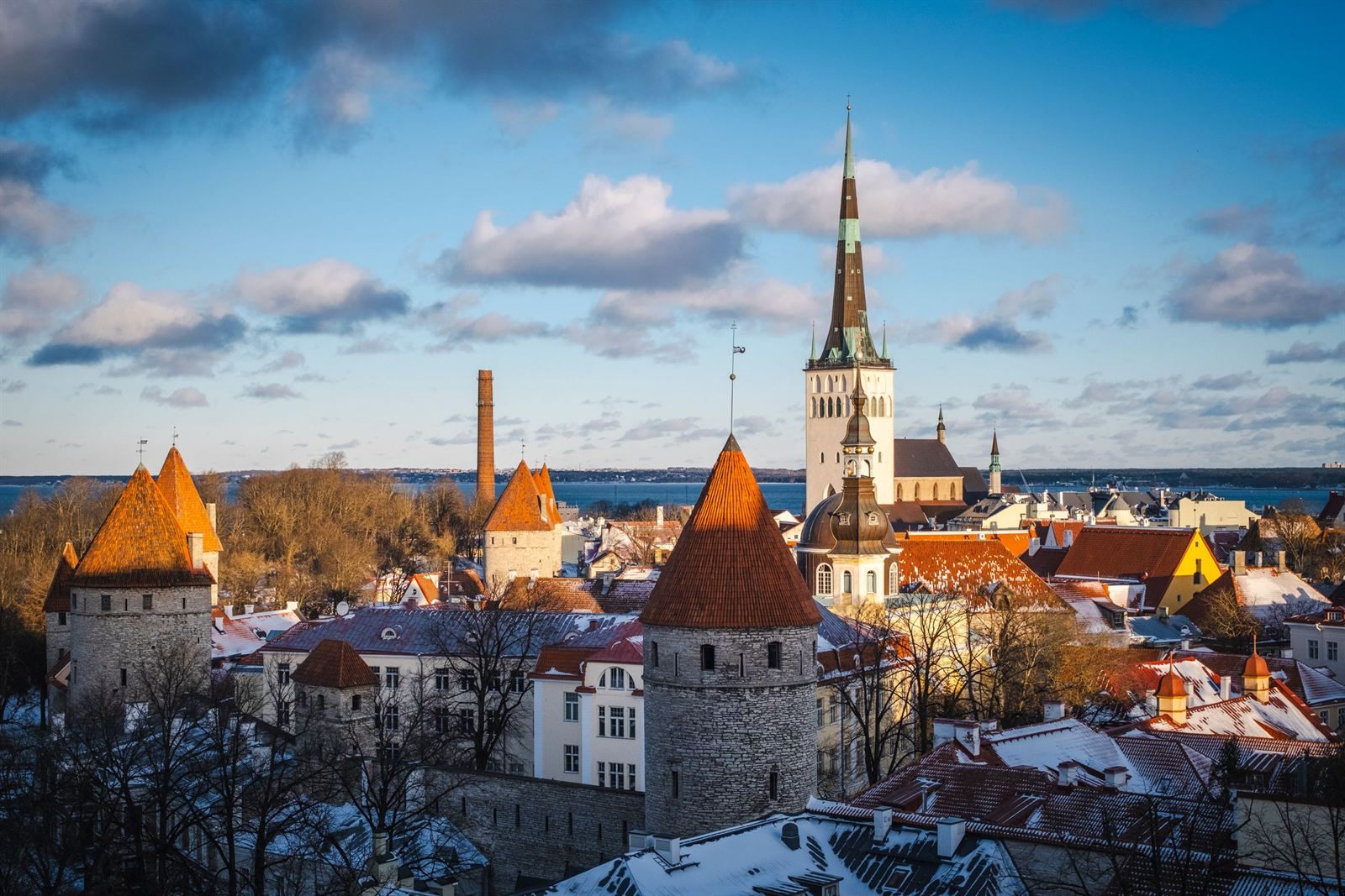 Red-roofed medieval towers and the tall church spire of Tallinn&rsquo;s Old Town, with light snow on the roofs